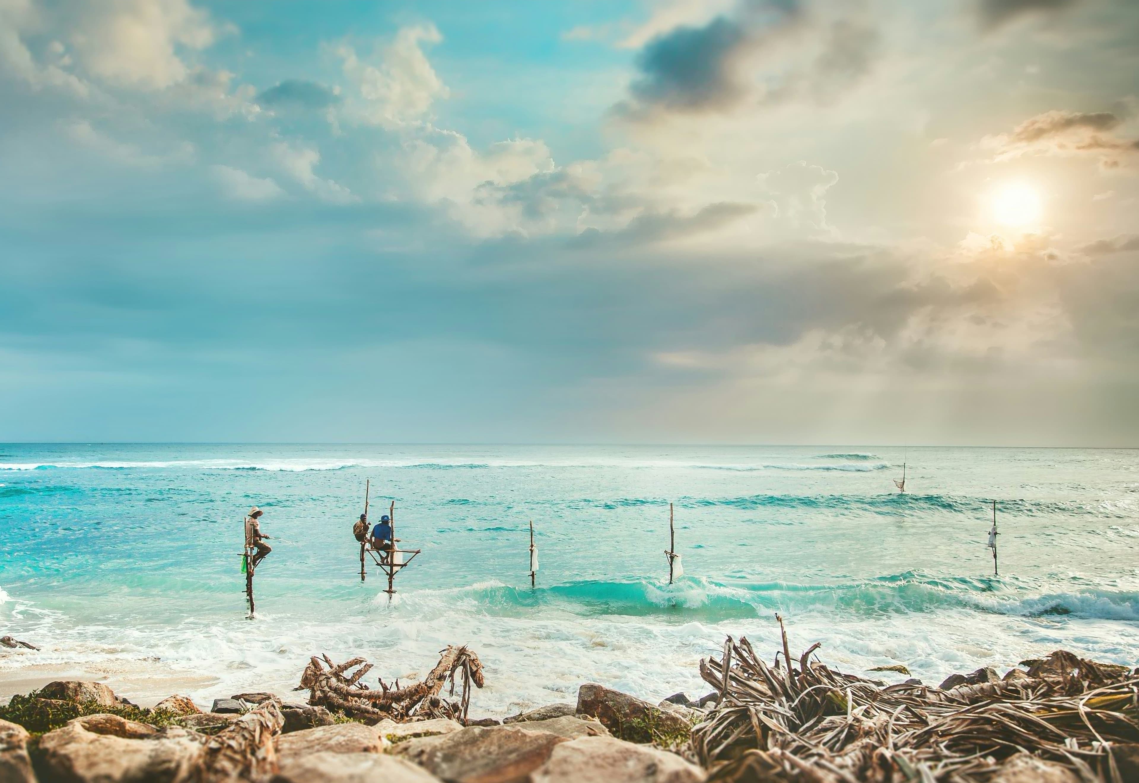 Sri Lankan fishermen perched on wooden stilts over breaking ocean surf.