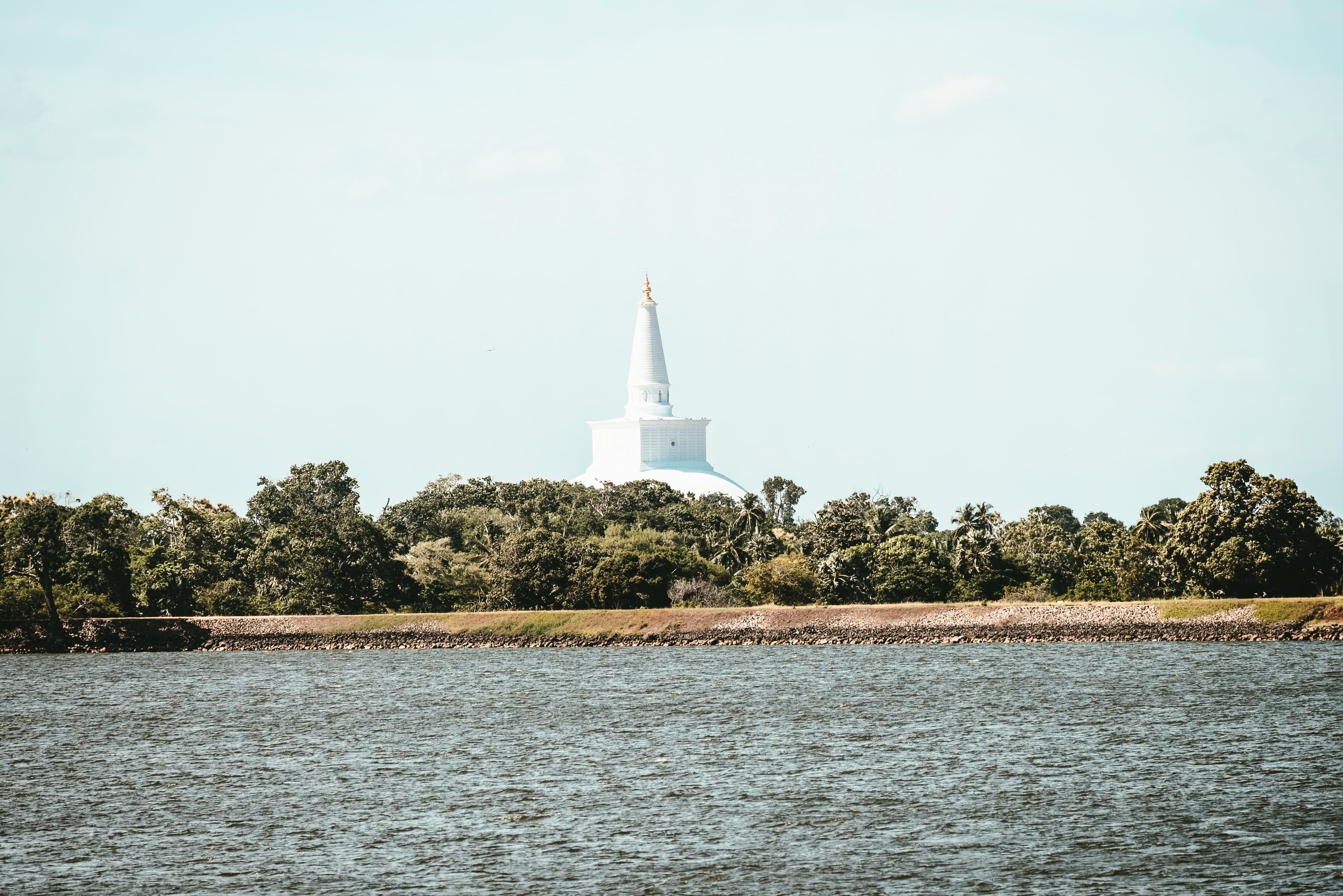 Pristine white bell-shaped stupa standing gracefully under clear tropical sky.
