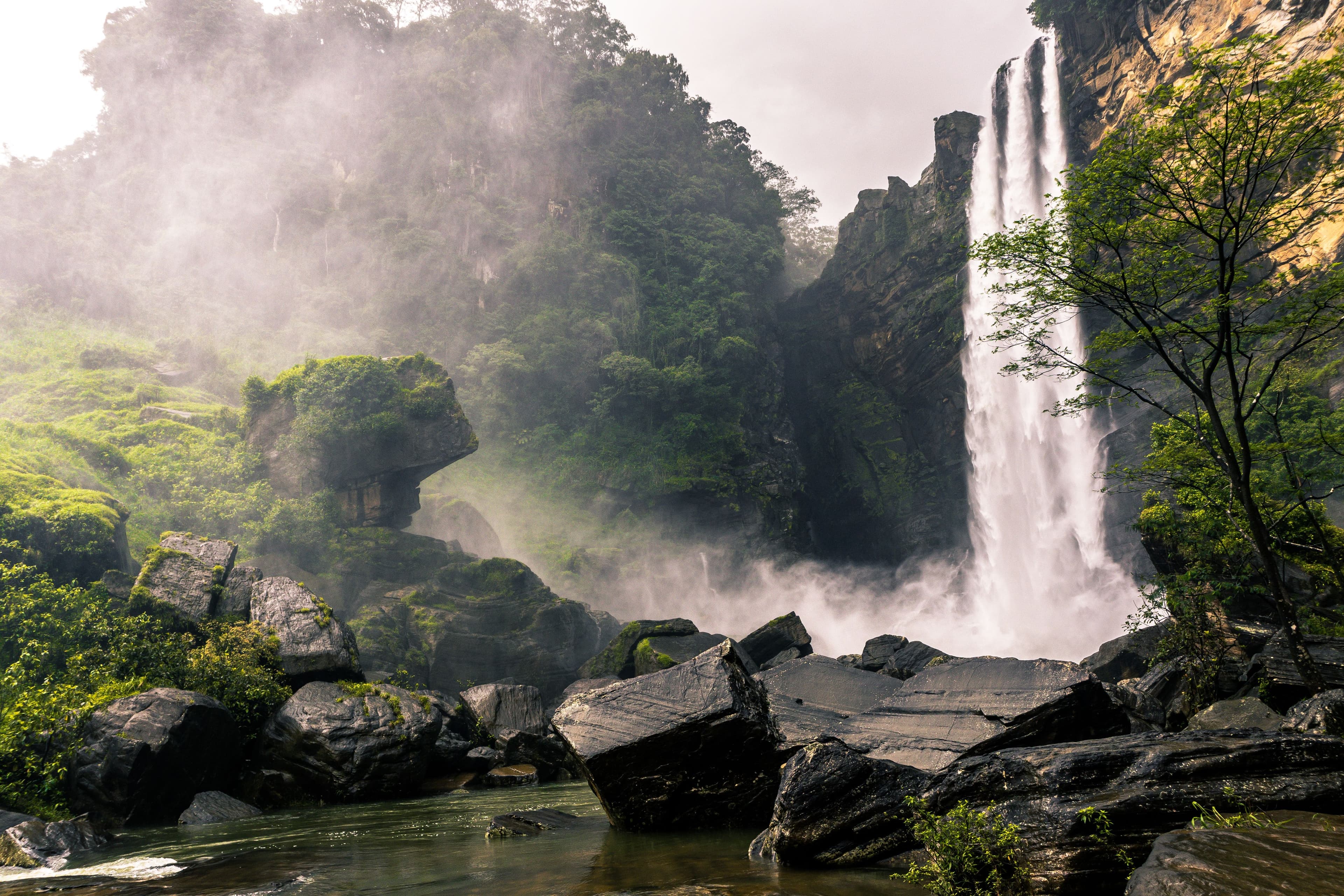 Wide mountain waterfall cascading into a crystal clear jungle plunge pool.
