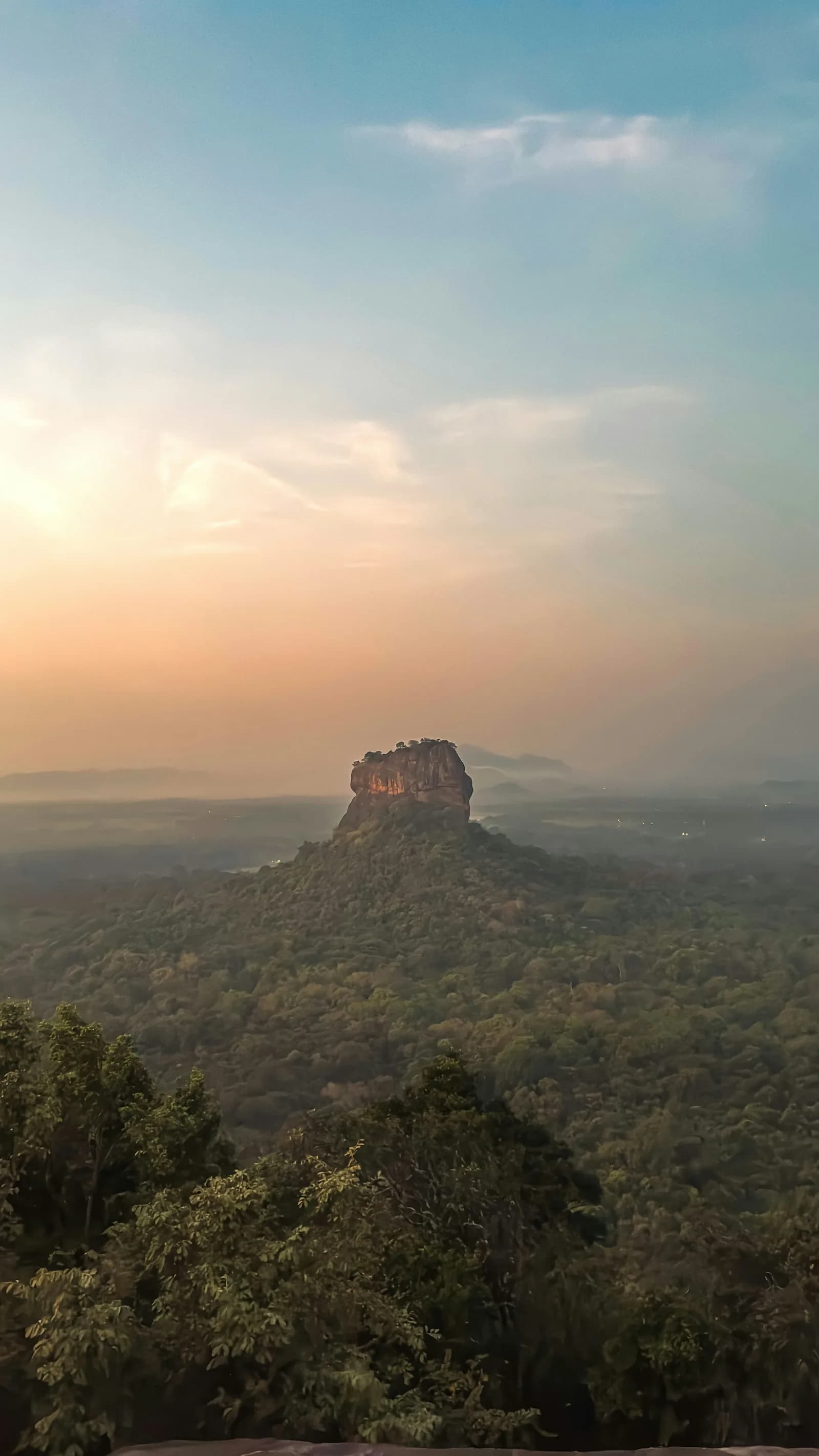Sigiriya rock rising dramatically out of morning jungle mist viewed from Pidurangala